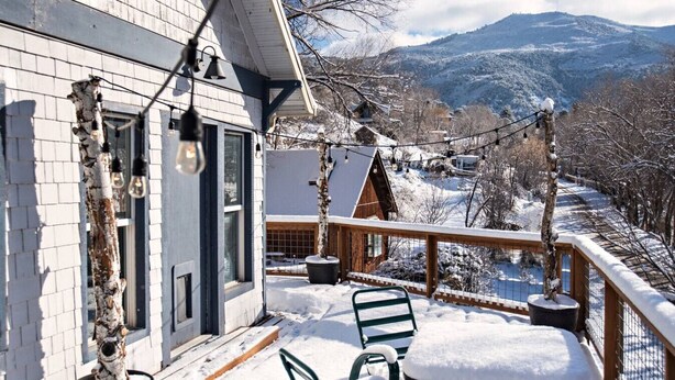 A snow-covered deck with a table and chairs, overlooking a snowy landscape with mountains in the background. - Historical, Renovated Home In Downtown, Near Pools (Glenwood Springs)