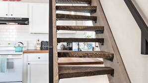 A staircase with wooden steps and metal railings in a modern kitchen with white cabinets and a kitchen island. - Historical, Renovated Home In Downtown, Near Pools (Glenwood Springs)