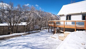 A snow-covered outdoor area with a wooden deck, a building with a white exterior, and bare trees. - Historical, Renovated Home In Downtown, Near Pools (Glenwood Springs)