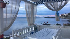 Un espace extérieur abrité, aménagé avec des sièges, et offrant une vue sur la mer et les collines lointaines.