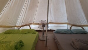Een tentachtige kamer met twee bedden, elk met een kussen, en een vloerventilator in het midden.