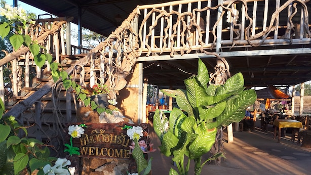 Een houten gebouw in rustieke stijl met een ‘WELCOME’-bord, omringd door bloempotten en bloemen.