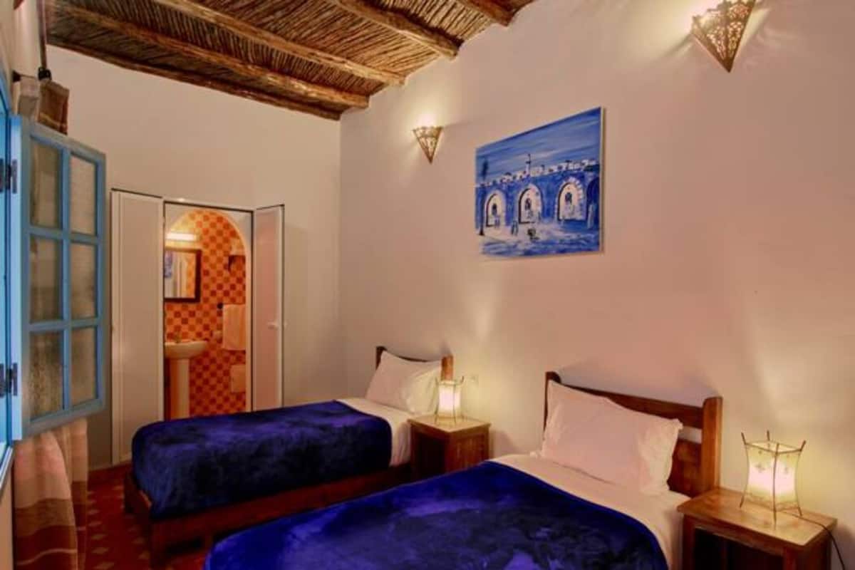 A room with two beds, a blue door, and a painting of arches on the wall.