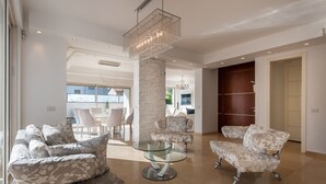 A modern living room with a glass coffee table, floral-patterned sofas, a hanging crystal chandelier, and a stone pillar. - Luxurious Villa with great location (Herzliya)
