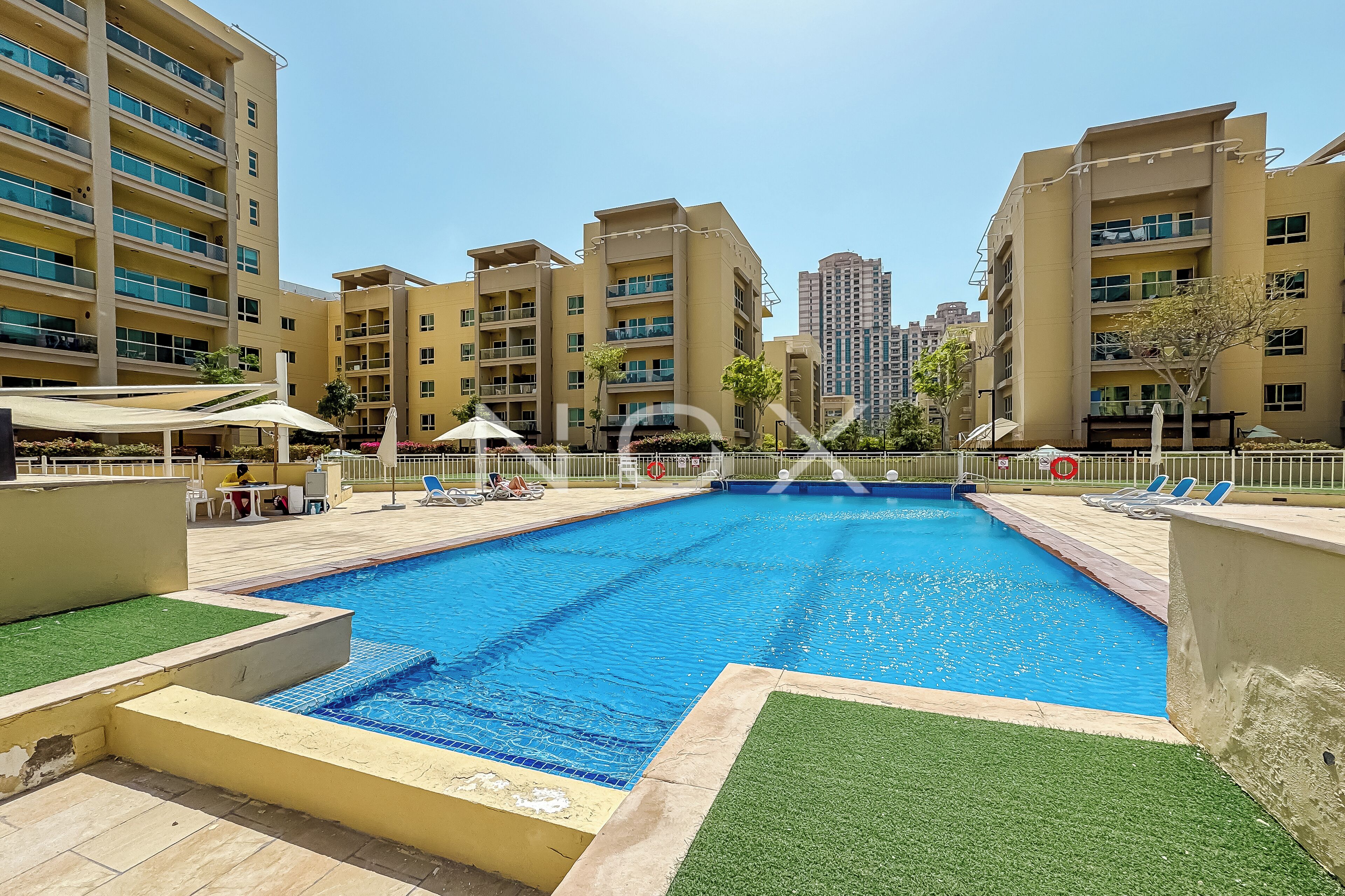 A swimming pool surrounded by apartment buildings, with sun loungers and umbrellas.