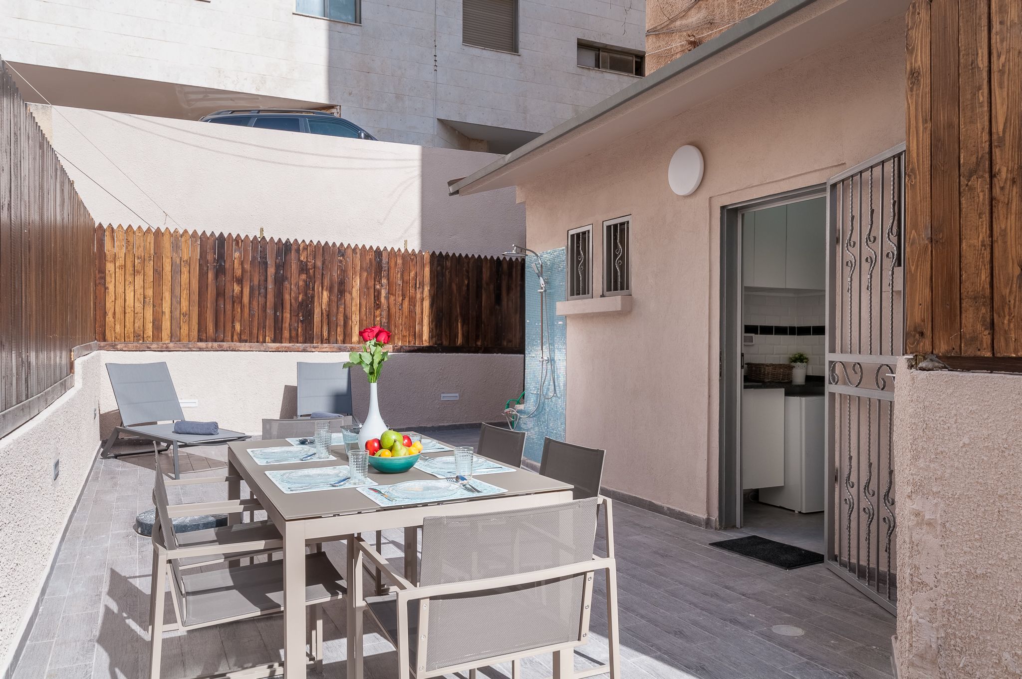 Un patio con una mesa para dos, un jarrón con flores y un edificio al fondo.