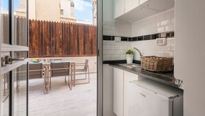Una cocina moderna con armarios blancos, una encimera negra y un refrigerador pequeño. Se ve un comedor con una mesa y sillas a través de una puerta de cristal.