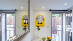 Un baño con un tocador blanco, un espejo y un estante amarillo con plantas en macetas.
