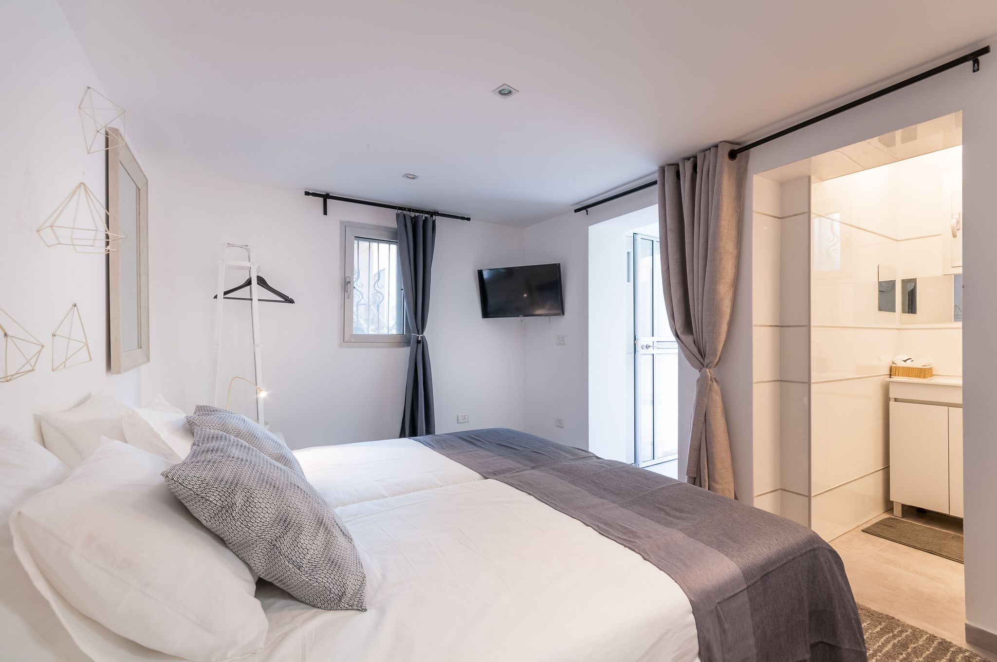 A modern hotel room with a large bed, a TV, a wardrobe, and a bathroom visible through an open door.