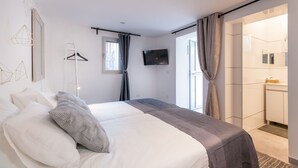 Habitación de hotel moderna con una cama grande, televisor, armario y baño visible a través de una puerta abierta.