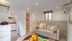 Una sala de estar moderna con un sofá, una mesa de comedor con fruta y una cocina al fondo.