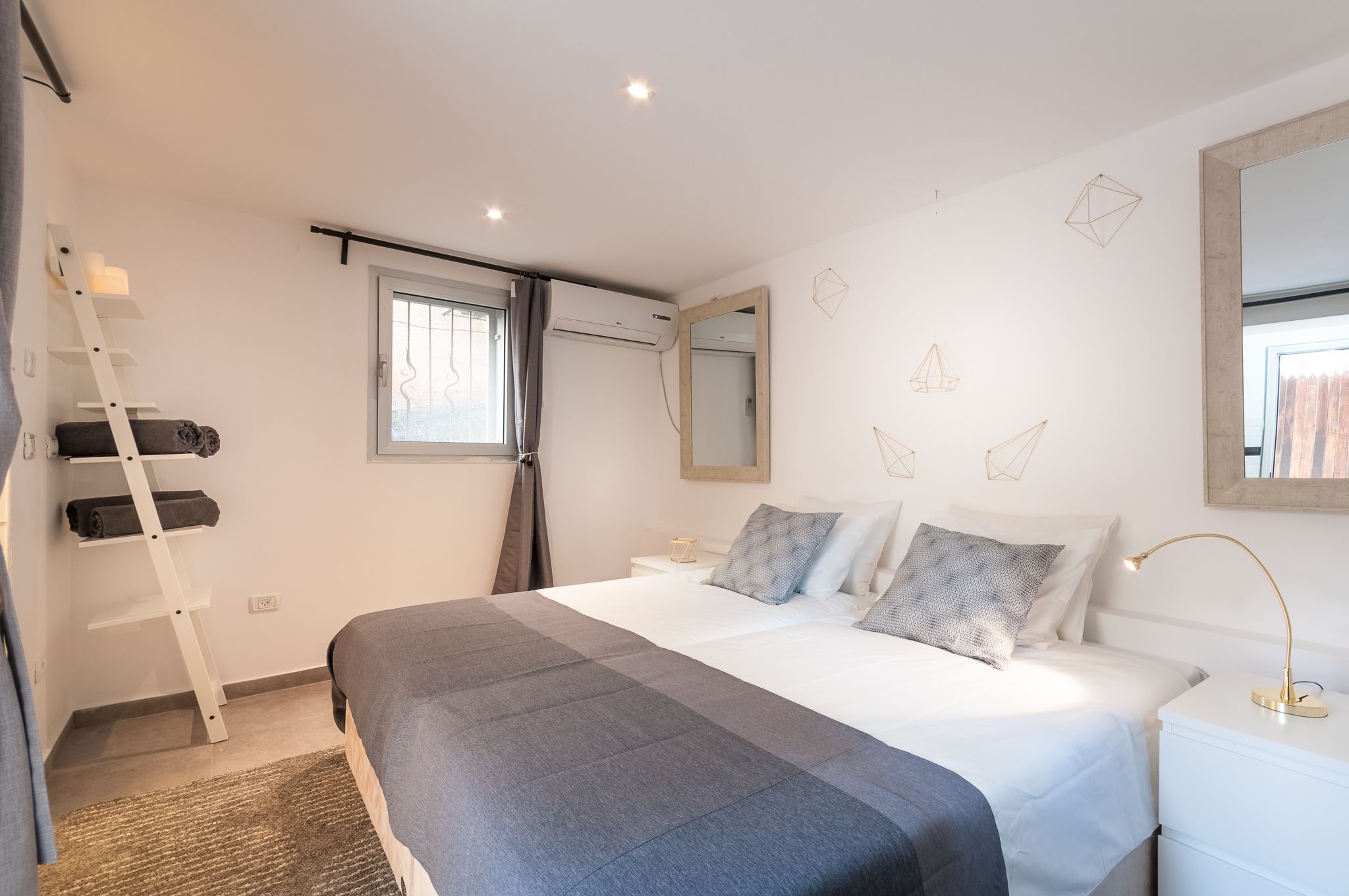 A modern bedroom with a bed, bedside tables, a ladder, a window, and a mirror.