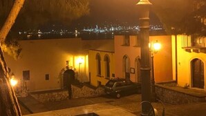 A nighttime view of a building with a stone staircase, a car parked in front, and a street lamp in the foreground. - L' Antico Borgo (Milazzo)