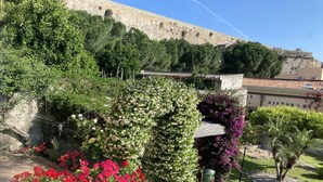 A garden with various plants and flowers, a stone wall, and a building with a sign that reads "Ristorante". - L' Antico Borgo (Milazzo)