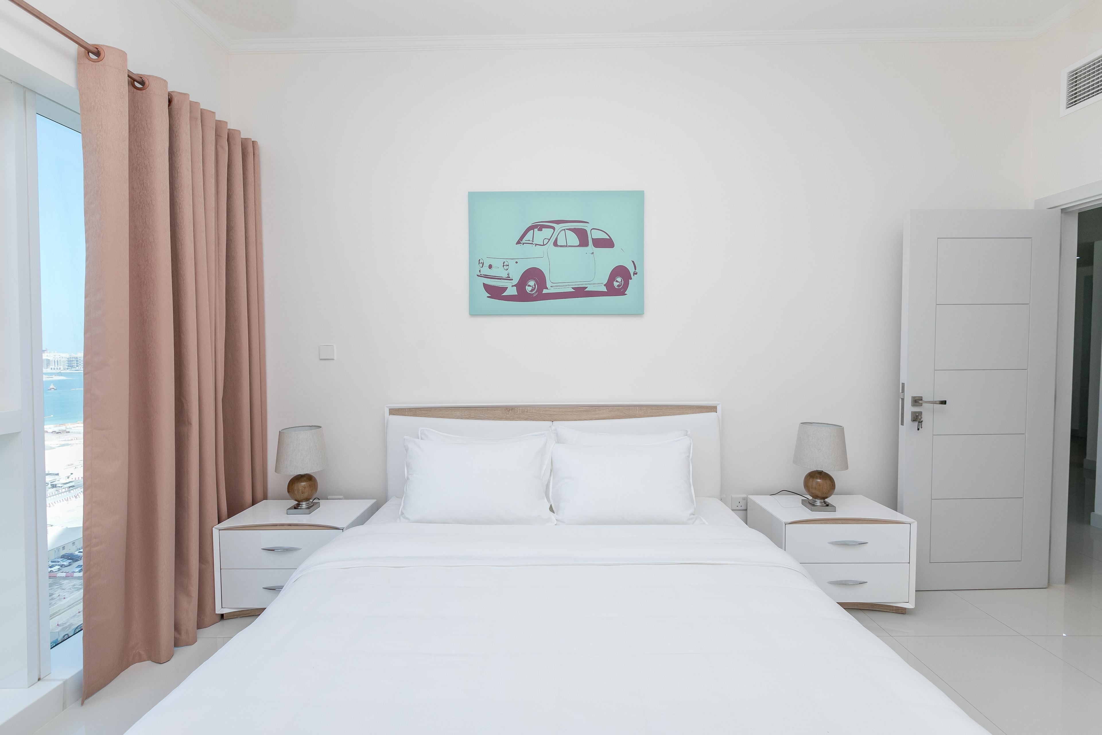 A bedroom with a bed, two bedside tables, a nightstand, a door, and a window with curtains.