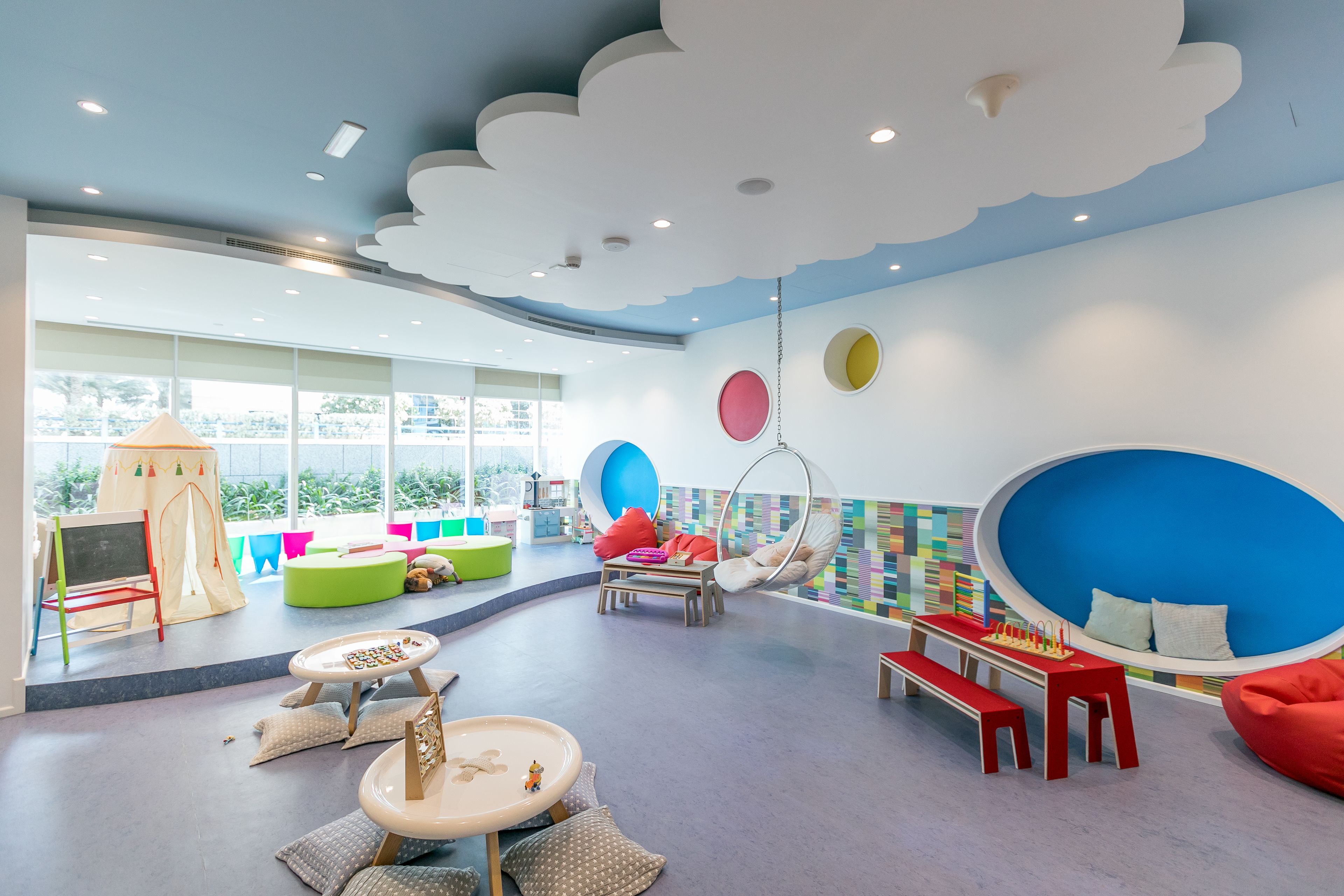 A children's playroom with a large window, colorful play area, and a hanging chair.