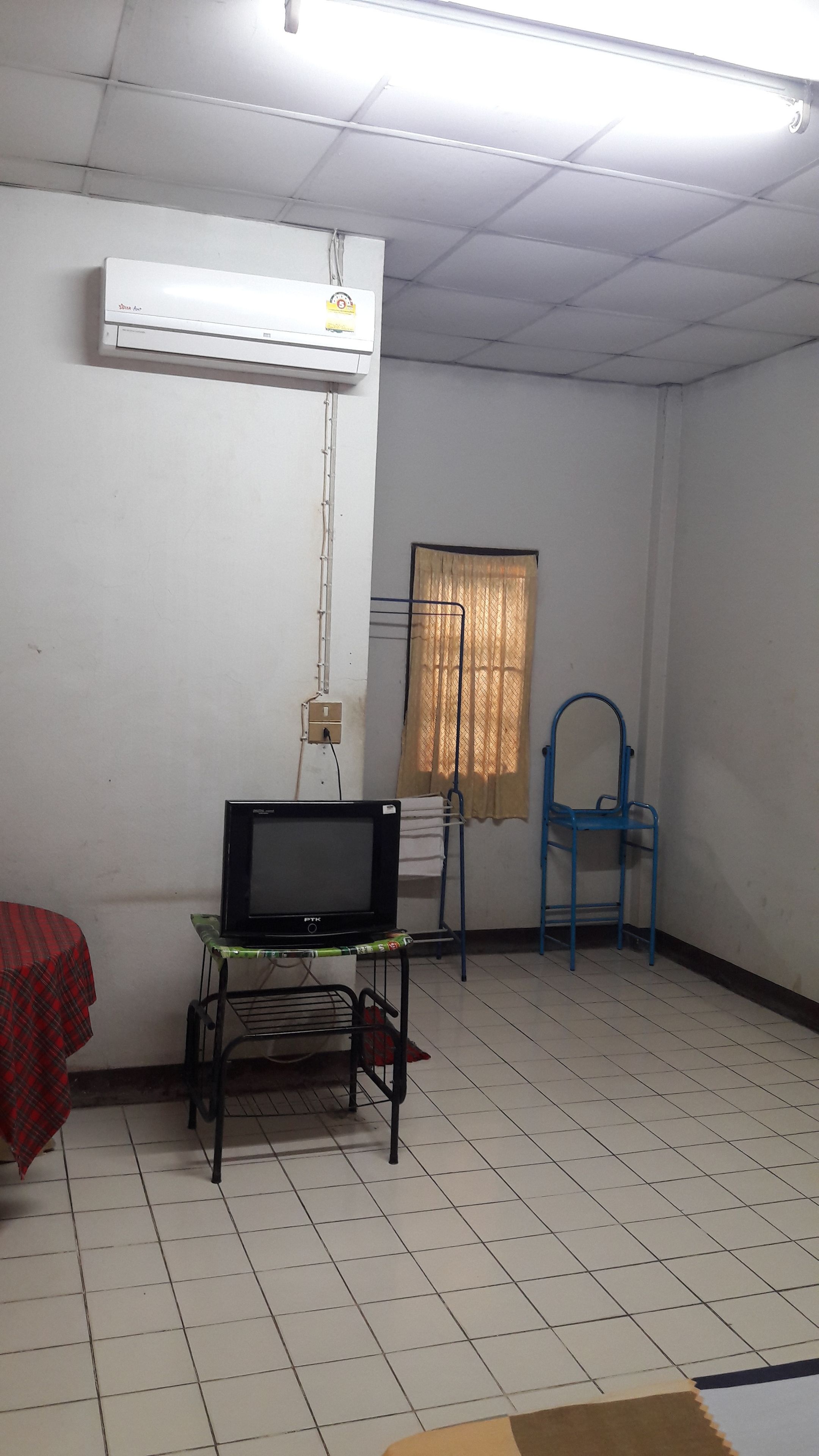 A room with a flat-screen TV on a stand, a blue chair, a window with curtains, and an air conditioning unit on the wall.