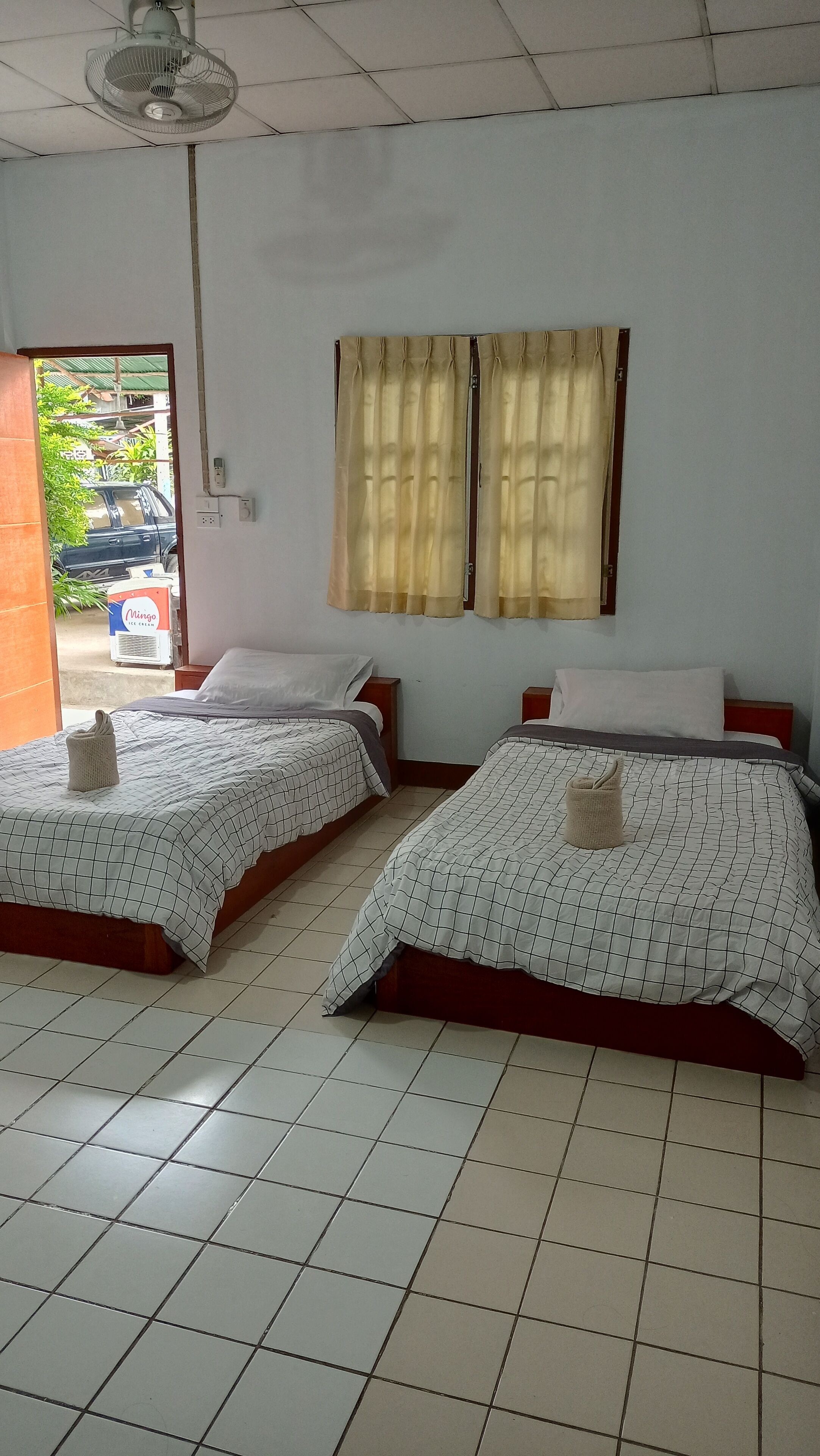 Ein Zimmer mit zwei Betten, einem Deckenventilator und einem Fenster mit Vorhängen.