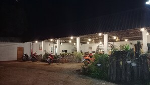 An outdoor covered area with seating and potted plants, a motorcycle, and a building in the background. - Vijitporn House Hotel (Mae Hong Son)