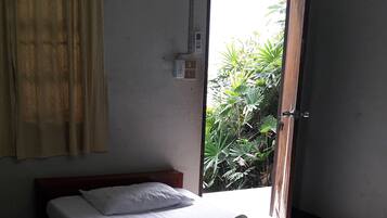 A single bed with a wooden headboard, a small bedside table, and a window with curtains.