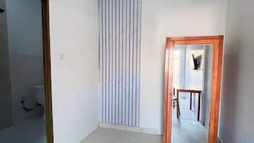Una habitación con piso de baldosas, cortina a rayas verticales, espejo con marco de madera y un baño con ducha a la vista.