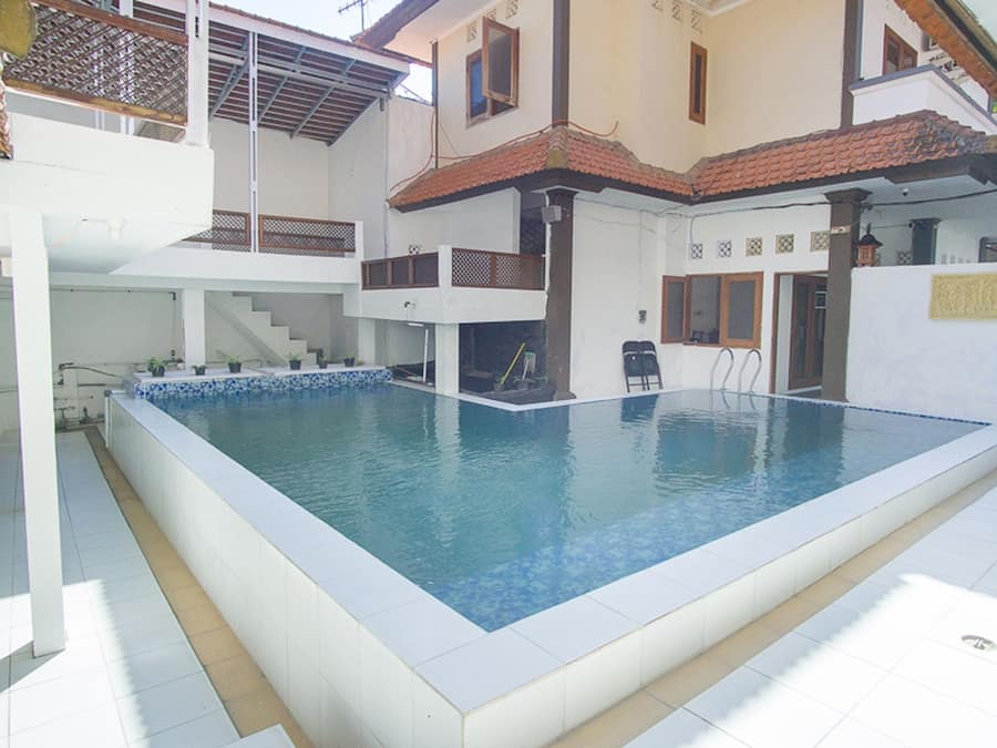 Piscina retangular com um deck ladrilhado ao redor, uma escadaria que leva a um nível superior e uma pequena área externa com assentos.