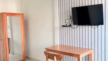 A room with a wooden table and chair, a television mounted on a striped wall, and a mirror cabinet.