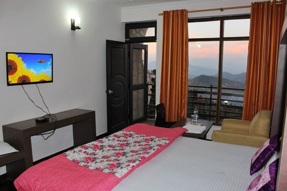 Ein Hotelzimmer mit Bett, Schreibtisch, Stuhl, Fernseher und einem Fenster mit Vorhängen.