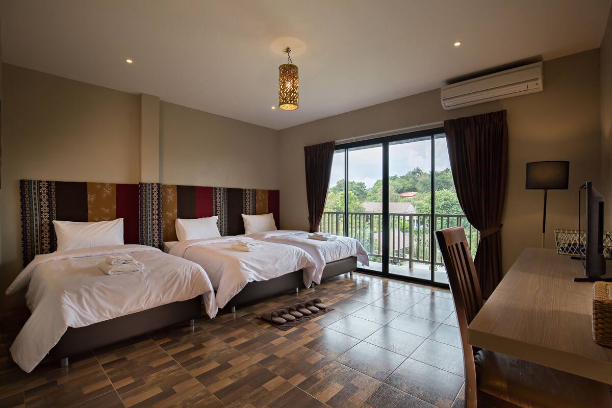 A hotel room with two beds, a balcony, a desk, and a TV.