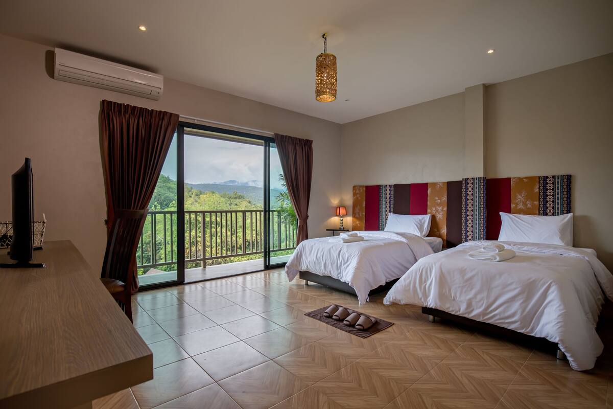 A hotel room with two beds, a TV, a balcony with a view, and a large window with curtains.