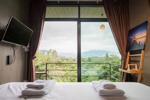 A hotel room with a large window, a bed with two towels, a TV on the wall, and a painting on the side. - Thanburi Resort (Chom Thong)