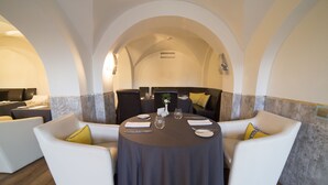 Un coin repas avec une table ronde dressée pour quatre personnes, entourée de fauteuils blancs agrémentés de coussins jaunes.