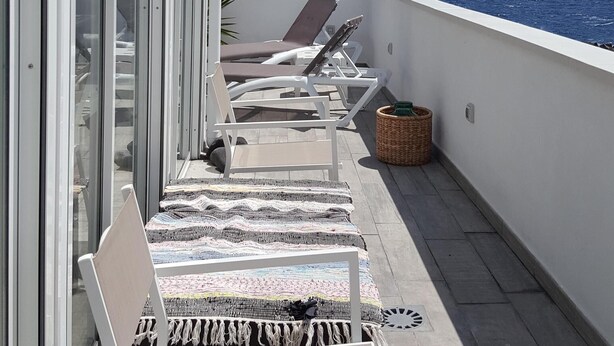 Ein Balkon mit weißen Korbstühlen, einem gemusterten Teppich und einer Palme.