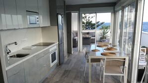 Eine moderne Küche mit einer großen Kochinsel, einem Essbereich mit Tisch und Stühlen sowie Meerblick durch große Fenster.