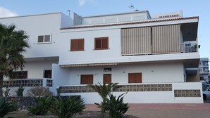 Ein modernes, zweistöckiges Gebäude mit flachem Dach, großen Fenstern mit Holzläden und einem Balkon mit Geländer.