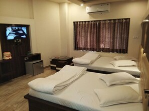A hotel room with two beds, a TV, a small desk, and a window with curtains. - Hotel Bani Hashim (Ajmer)