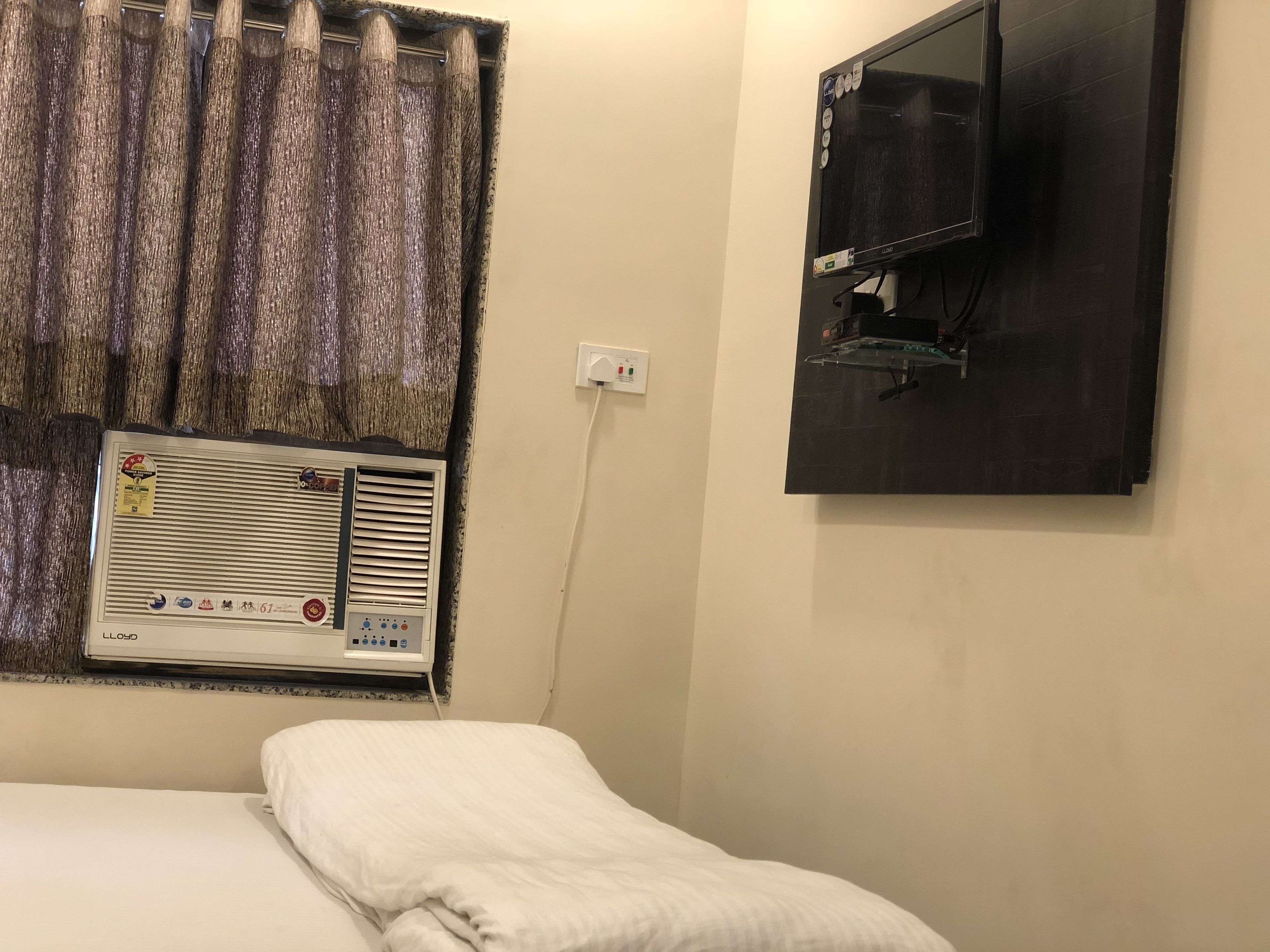 Una habitación de hotel con una cama, una ventana con cortinas, un aire acondicionado instalado en la pared y un televisor.