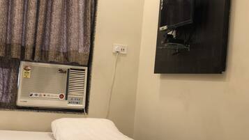 Una habitación de hotel con una cama, una ventana con cortinas, un aire acondicionado instalado en la pared y un televisor.