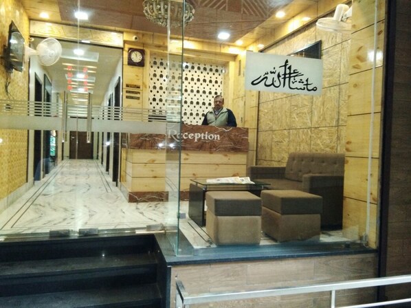 A reception area with a marble floor, a reception desk, and a seating area with ottomans. - Hotel Bani Hashim (Ajmer)
