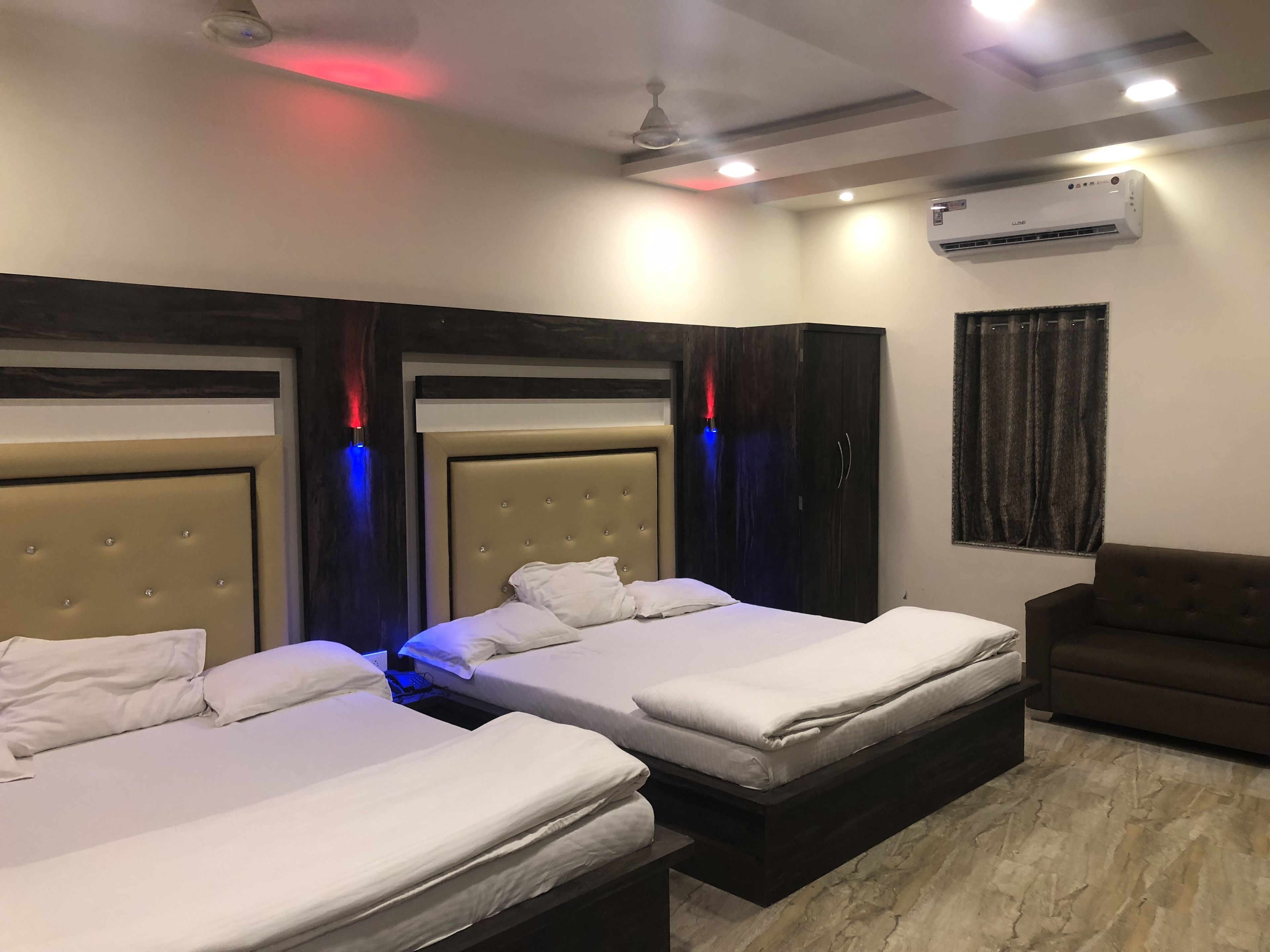 A hotel room with two beds, a dark-colored sofa, an air conditioning unit, and a window with curtains.