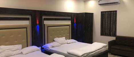 A hotel room with two beds, a dark-colored sofa, an air conditioning unit, and a window with curtains.