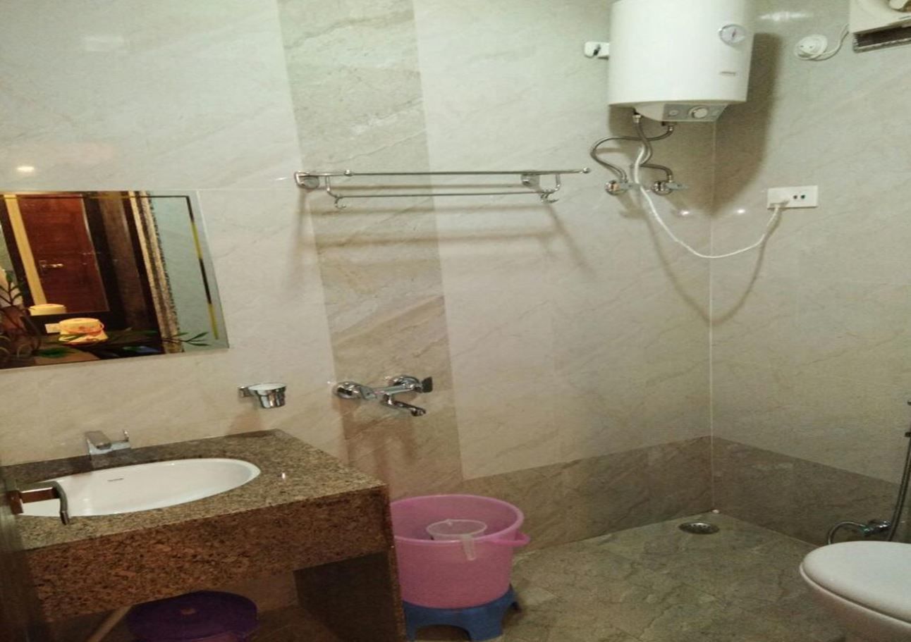 Un baño con lavamanos de encimera de granito, un espejo, toallero, ducha y retrete.