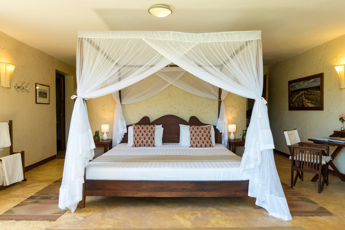 A four-poster canopy bed with white bedding, two decorative pillows, bedside lamps, and a wooden nightstand.