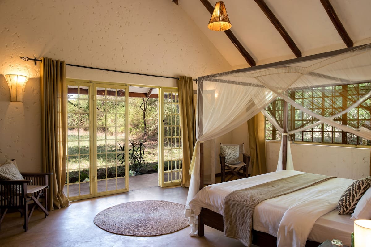A bedroom with a bed, a round rug, a chair, a bench, and a window with curtains.