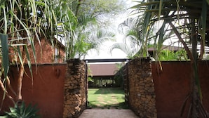A stone archway leading to a covered patio area with a stone wall and tropical plants. - Kili Villa (Arusha)