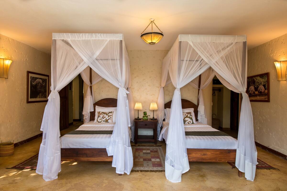A room with two beds, each with a canopy, a nightstand with lamps, and a patterned rug.