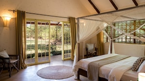 A bedroom with a canopy bed, a round rug, and a view of the outdoors through a glass door. - Kili Villa (Arusha)