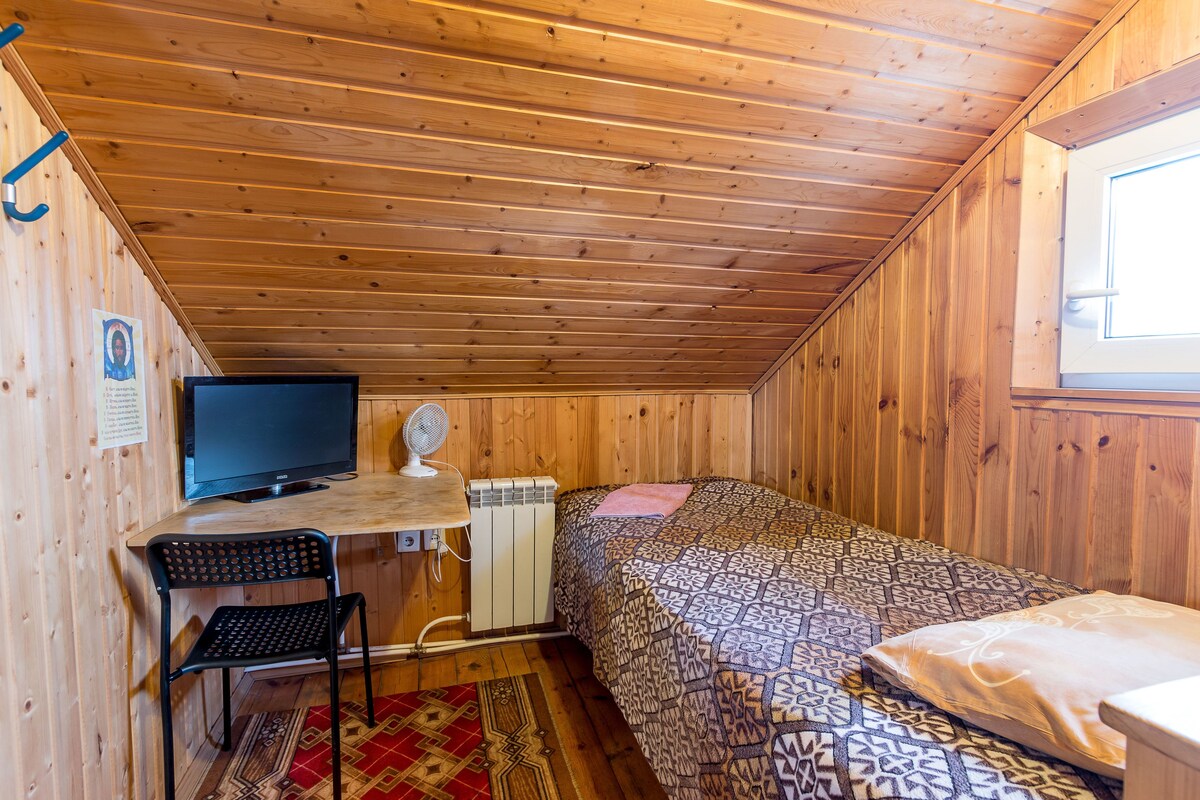 Une pièce aux murs lambrés, comprenant un lit, un bureau avec un ordinateur, une chaise et un radiateur.