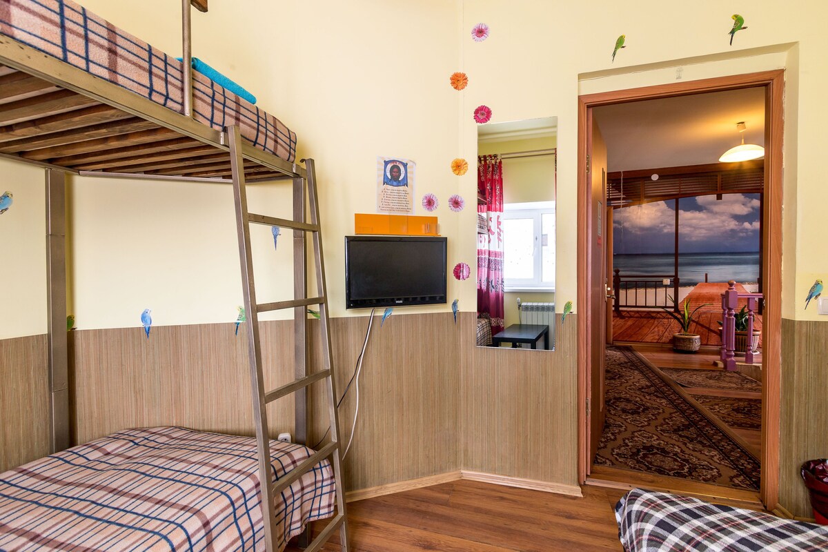 Une chambre avec un lit superposé, un bureau avec un ordinateur, une télévision et une vue sur l’océan, visible par la porte.