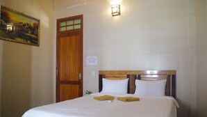 Una habitación de hotel con puerta de madera, una cama con ropa blanca y un cuadro en la pared.